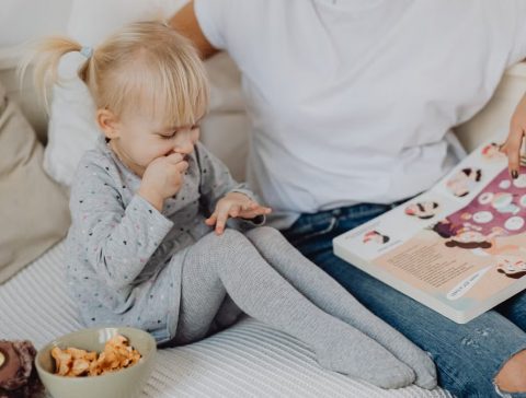 A mother and daughter enjoying storytime on a cozy couch with snacks nearby.